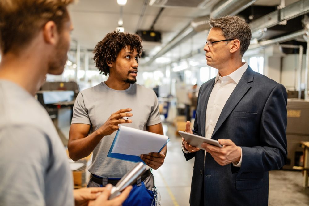 African American worker talking with a manager while going through reports in steel factory.