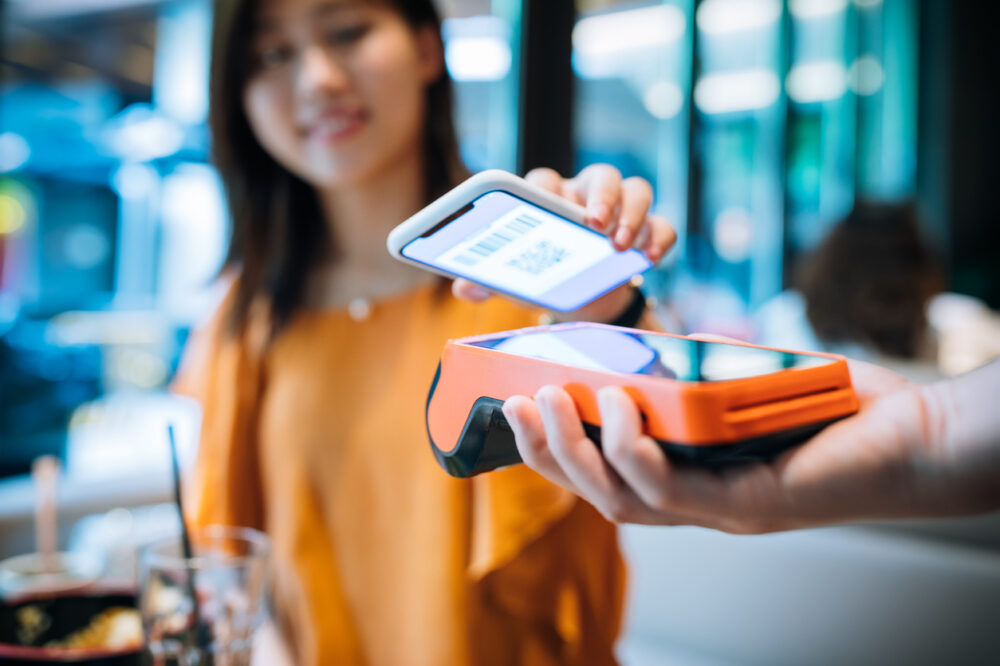 Asian young woman paying with smartphone in a cafe