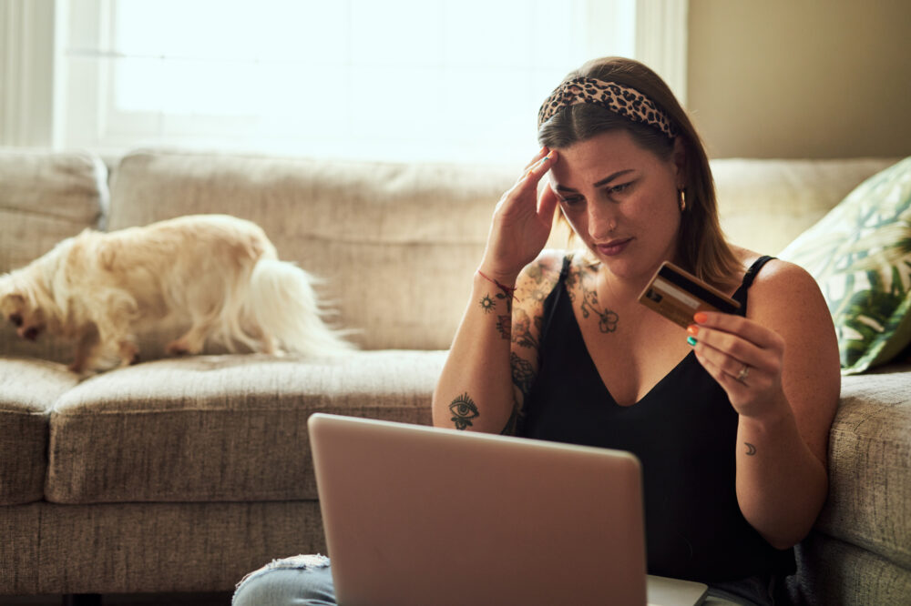 Shot of a young woman looking stressed while using a laptop and credit card at home