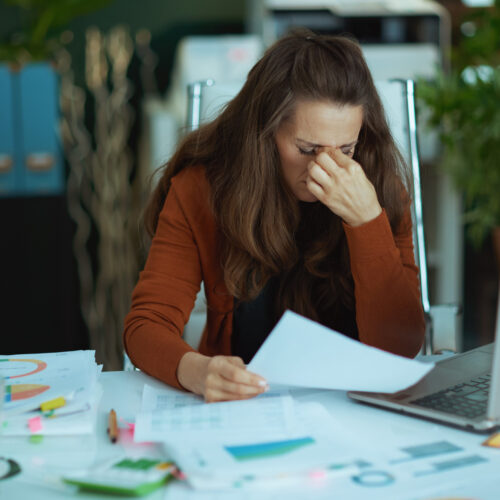 Woman small business owner with documents and laptop looking stressed