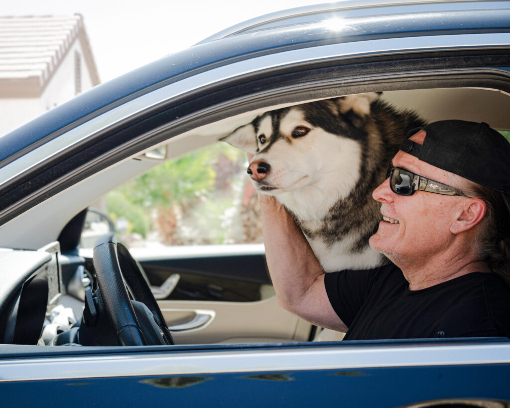 Current photo of Rob driving in the car with the husky that he adopted.