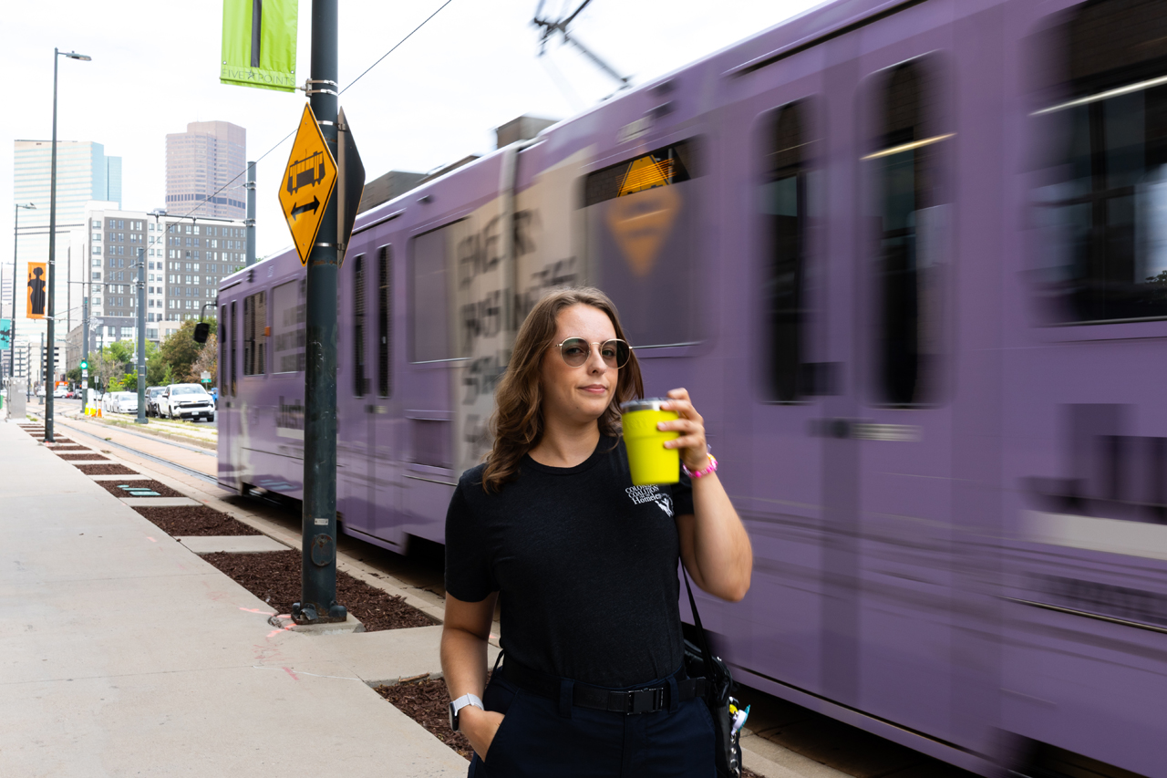 Angel drinks a takeout coffee while a purple train passes behind them