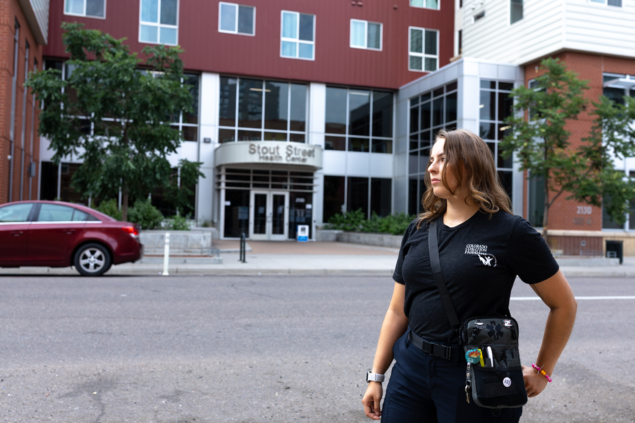 Angel stands outside of Stout Street Health Center wearing her Colorado Coalition for the Homeless uniform