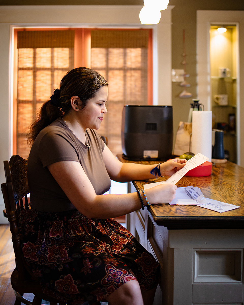 Profile shot of Rebecca at her desk looking over bills
