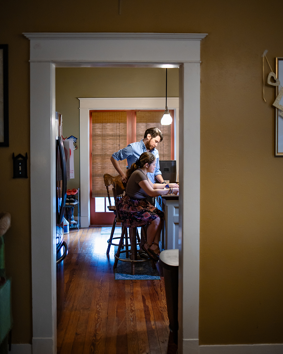 Faraway shot of Rebecca and her husband looking over bills in the kitchen