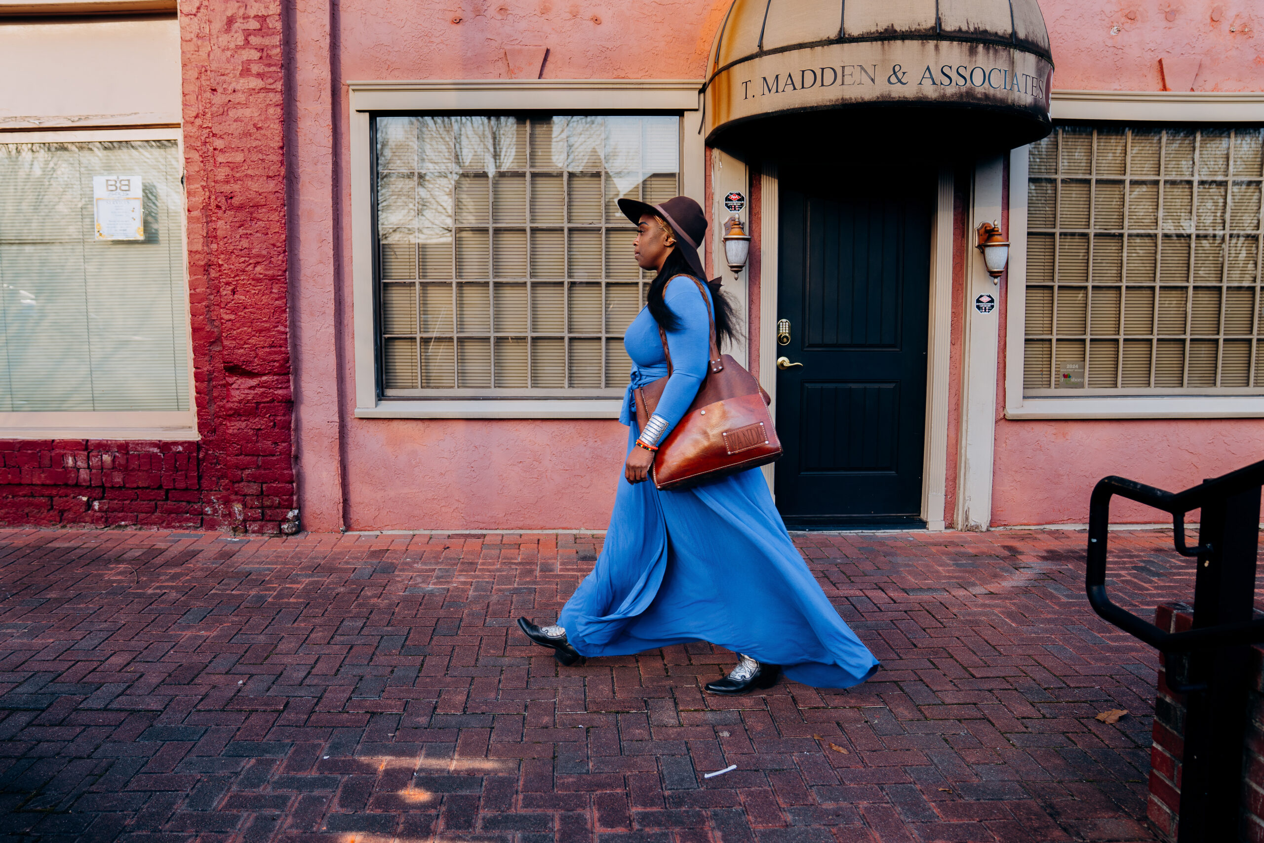 Wande walks down the sidewalk in front of old businesses