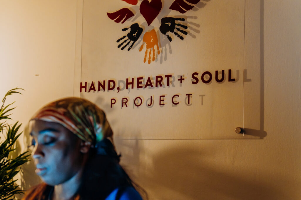 Wande works at her desk in front of the Hand, Heart + Soul Project logo