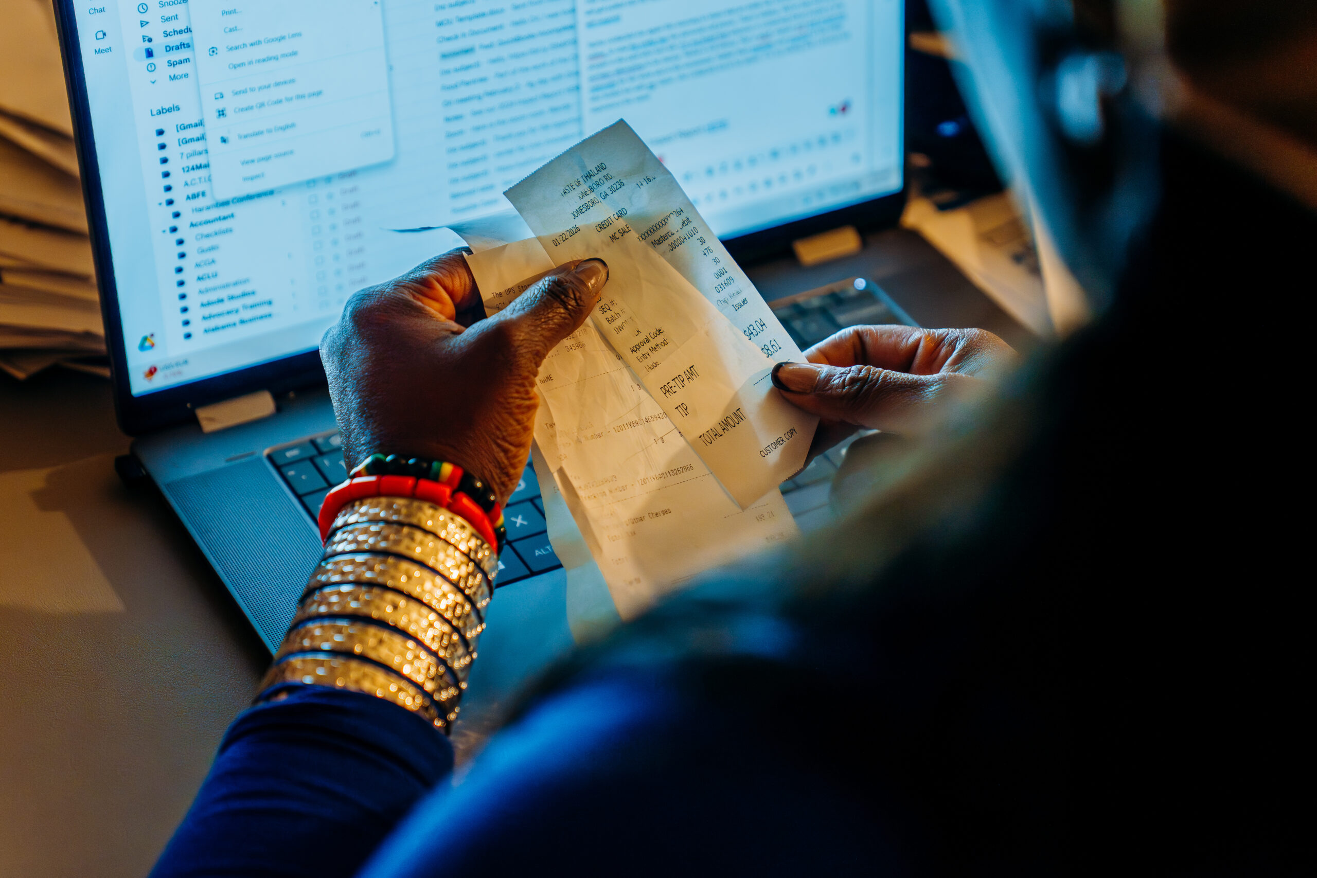 Wande sits at her computer and looks at receipts in her hands