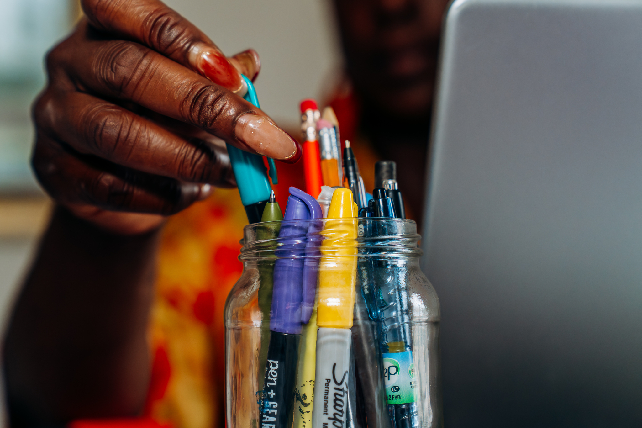 closeup of Ori's hand grabbing a pen from a jar full of pens