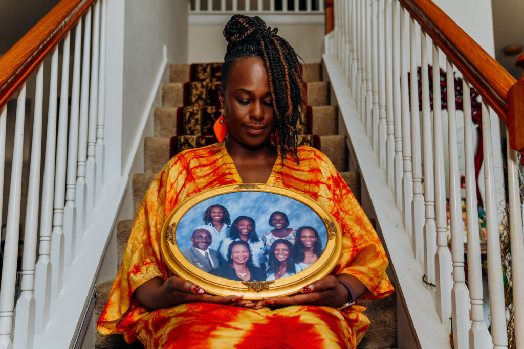 Ori sits on the staircase at her home holding a framed family portrait