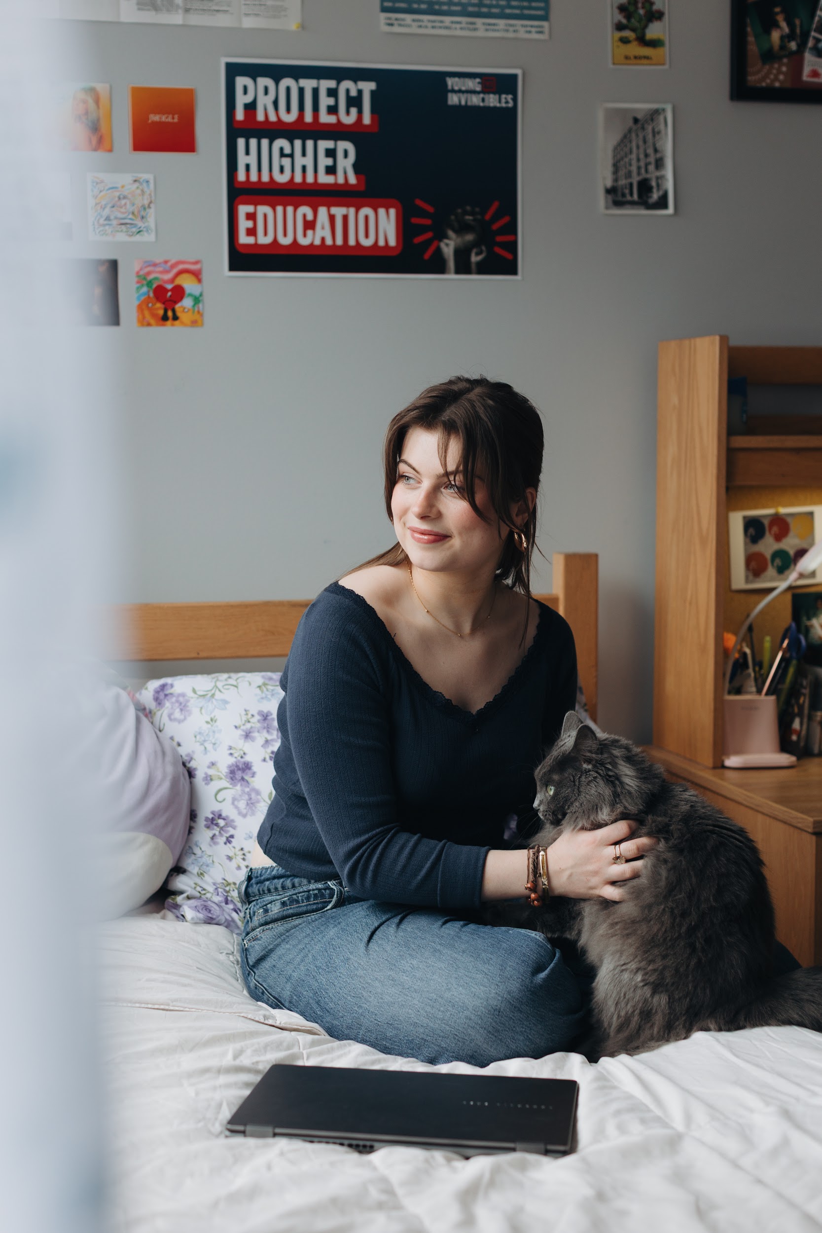 Margarita sits on her bed, petting her cat and looking out the window