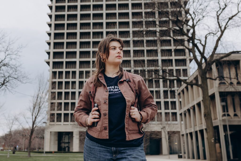 Margarita stands outside with her bookbag on with her school building in the background