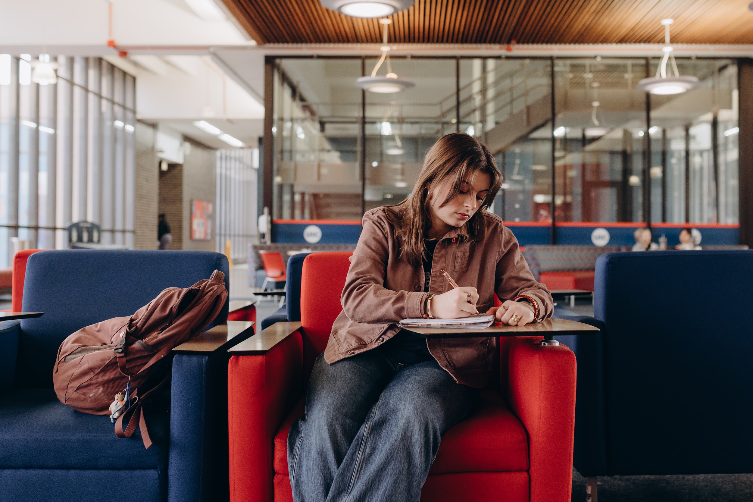 Margarita sits in a red desk chair in the student commons and writes in her notebook