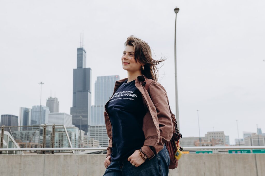Margarita stands on the roof of a parking deck looking off in the distance and smiling with the city of Chicago in the background