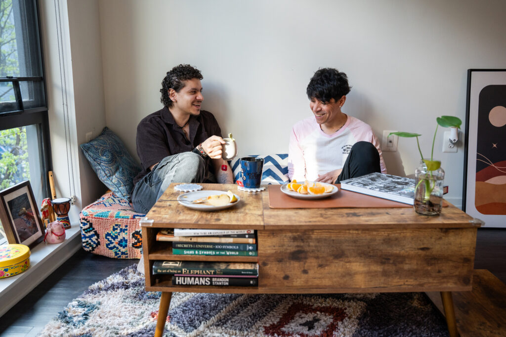 Yousef has snacks and tea with a friend in his living room. They talk and laugh