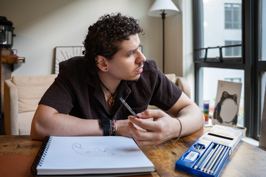 Yousef pauses from working in his sketchbook at home to look out the window