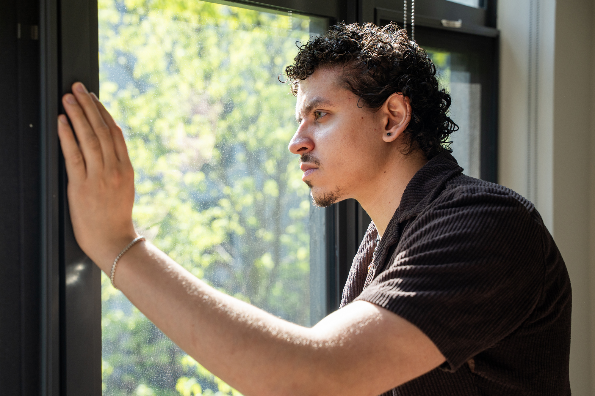 Yousef looks out the window of his apartment resting his hand on the frame