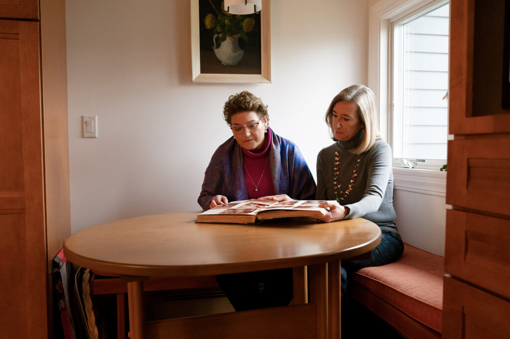 Linda and Elizabeth sit at the kitchen table and look through a photo album